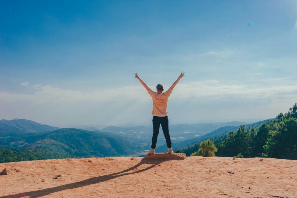 A woman stands victoriously on a mountain top with arms raised, embracing nature and freedom.